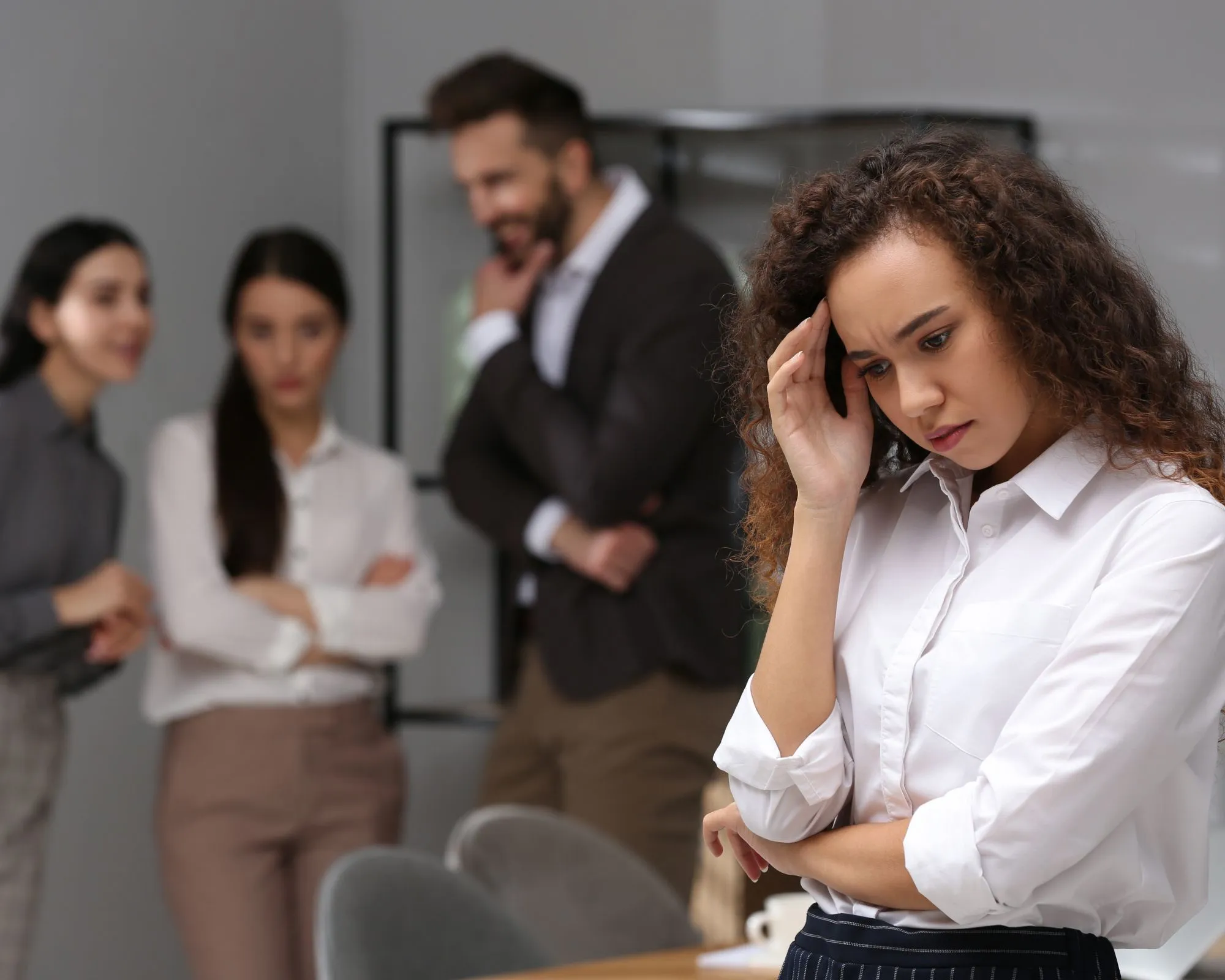 A distressed young woman at work while coworkers whisper behind her